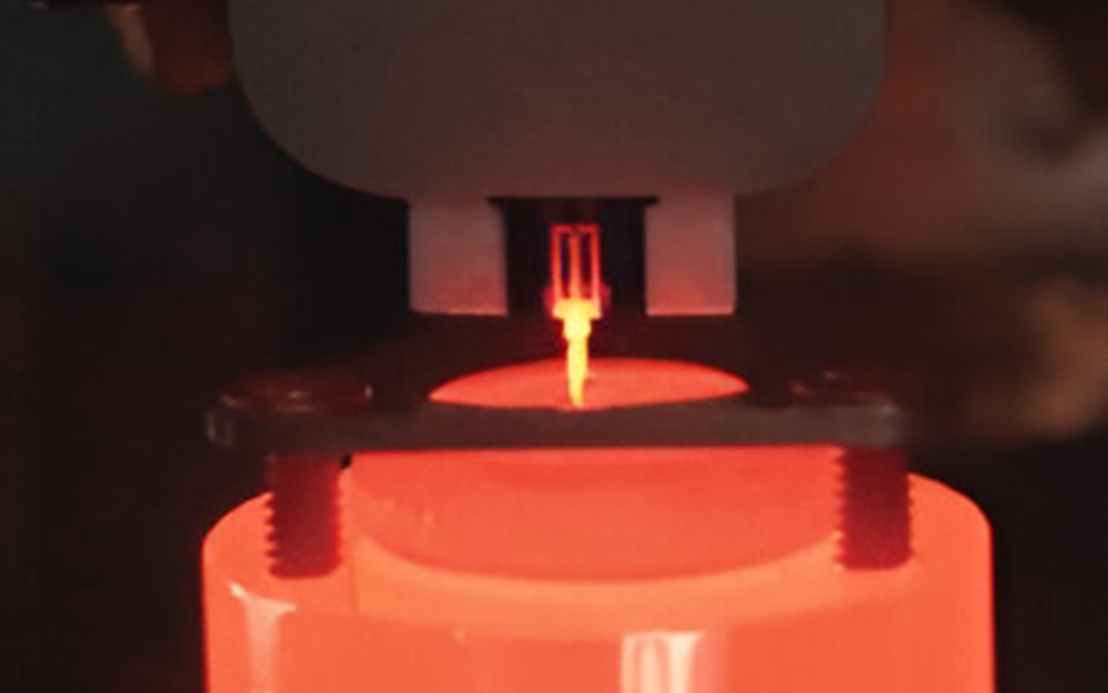 <p>Close-up view of nanoindentation test with a glowing indenter tip during high-temperature testing.</p>
