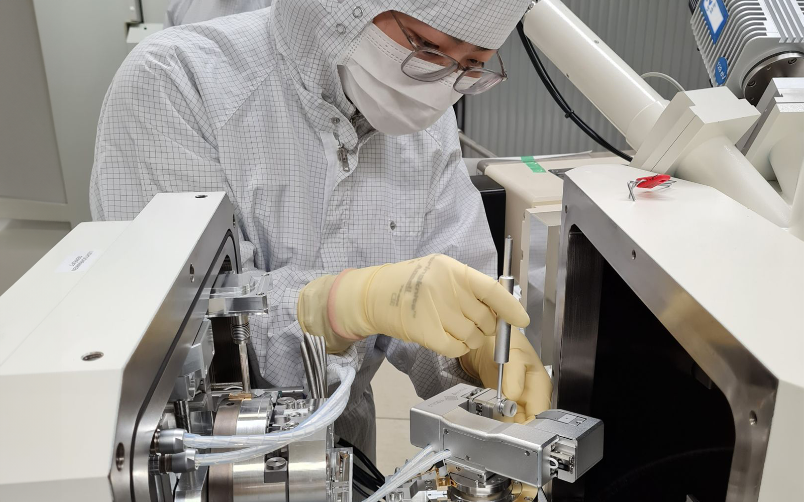 <p>Technician in cleanroom suit installing NMT04 nanoindenter in a SEM.</p>
